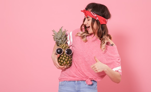 Portrait of hipster girl and pineapple isolated on pink wall