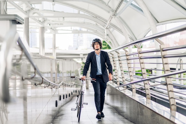 Il ritratto dell'uomo d'affari bello dei pantaloni a vita bassa in vestito con lo zaino cammina e tiene la bicicletta di guida sulla via della città della via andare al concetto della bici di trasporto di viaggio di lavoro di lavoro