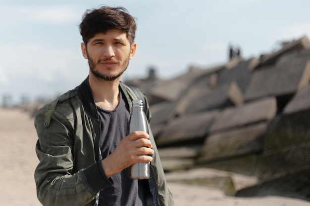 Portrait of hipster with steel thermo bottle for water in hand.