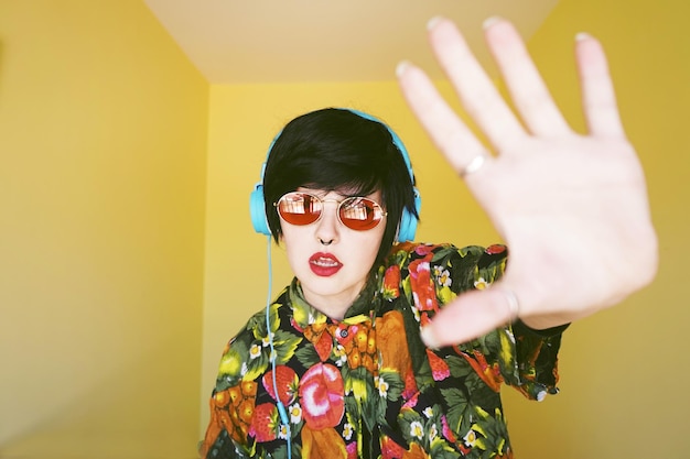 Photo portrait of hipster woman listening music against yellow wall