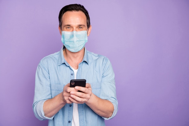 Portrait of his he mature guy using device browsing news cov mers flu pandemia wuhan china infection wearing safety gauze mask isolated over purple lilac violet color background