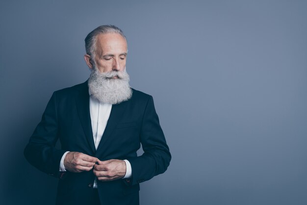 Portrait of his he nice attractive chic classy serious content minded gray-haired man macho wearing tux fastening button preparing isolated over dark grey pastel color background