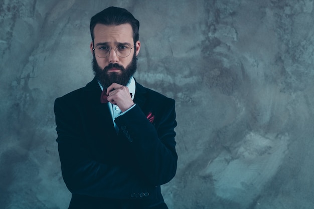 Portrait of his he nice attractive well-dressed sad bearded guy wearing tuxedo thinking isolated over gray concrete industrial wall