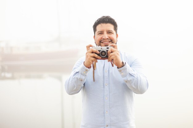 Portrait of hispanic guy with retro camera foggy weather