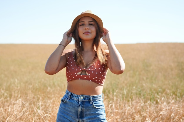 Portrait of a Hispanic woman wearing a hat posing on a wheat field on a sunny day