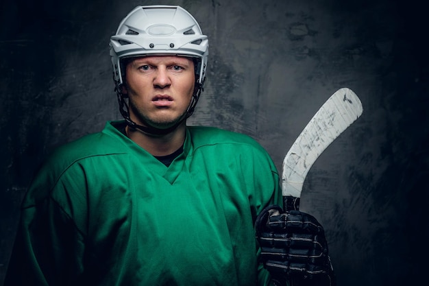 Photo portrait of a hockey player in protective clothes holds playing stick on grey background.