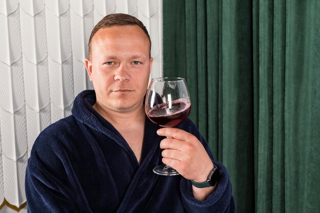 Foto ritratto un uomo casalingo in un accappatoio blu un uomo di mezza età con un bicchiere di vino rilassante dopo il lavoro