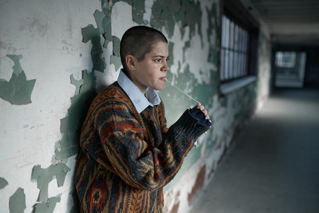 Portrait of homeless hipster teenager woman with short hair chewing gum looking aside. Poor teen girl wearing ragged clothes