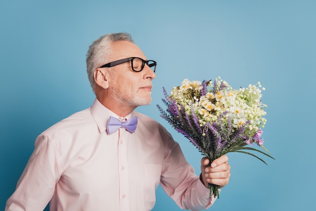 Portrait of husband aged guy with wild flowers bunch prepare for date ob blue background