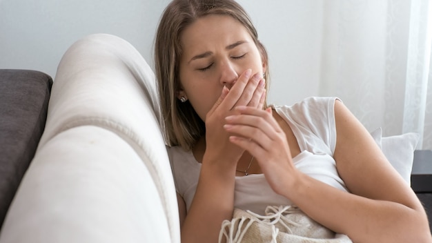 Portrait of ill woman with virus lying on sofa and coughing