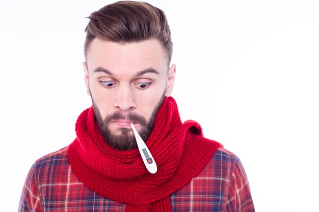 Portrait of ill young bearded man wrapped in scarf measures temperature trembles from cold stay at home has sick look tries to break fever takes remedies Seasonal flu Healthcare