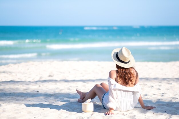 Portrait image of a beautiful asian woman enjoy sitting and drinking coconut juice on the beach