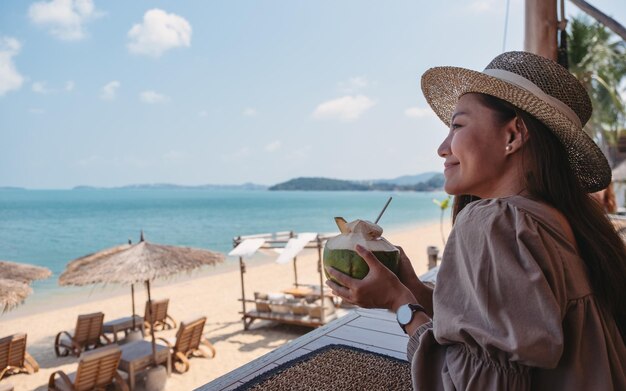 Portrait image of a beautiful young asian woman holding and drinking coconut juice in the beach cafe