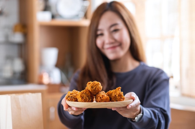 Portrait image of a beautiful young asian woman holding and showing a plate of fried chicken in the kitchen at home