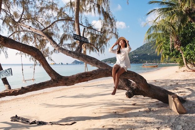 Portrait image of a beautiful young asian woman sitting on the tree by the sea