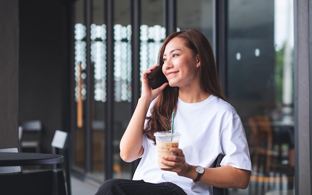 カフェでコーヒーを飲みながら携帯電話で話している美しい若いアジアの女性の肖像画の画像