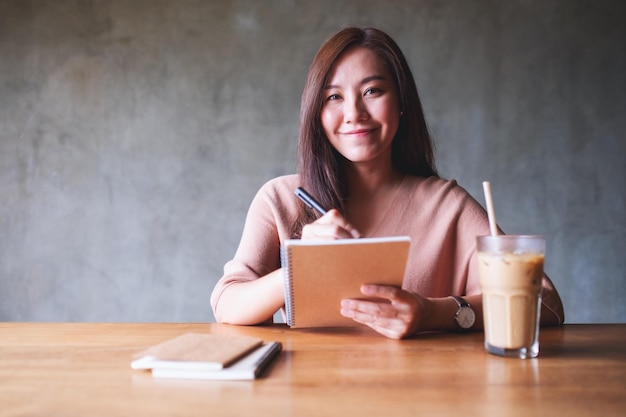 働いてノートに書いている美しい若いアジアの女性の肖像画の画像