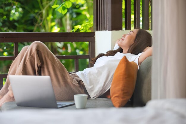 Photo portrait image of a young woman laying down on sofa with laptop computer and coffee cup