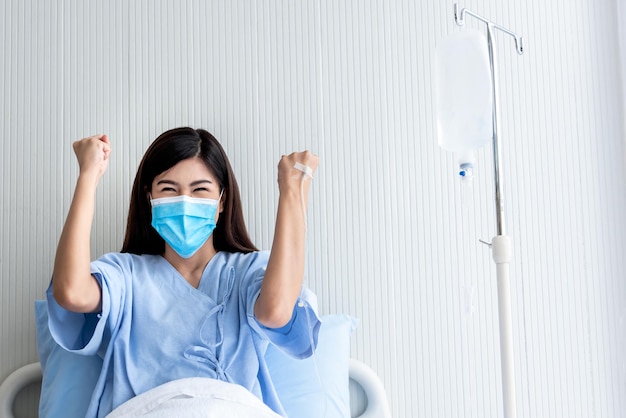 Portrait images of Asian attractive woman patient wearing a surgical mask sitting in patient's bed, having good treatment satisfaction, to people health care and health insurance concept.