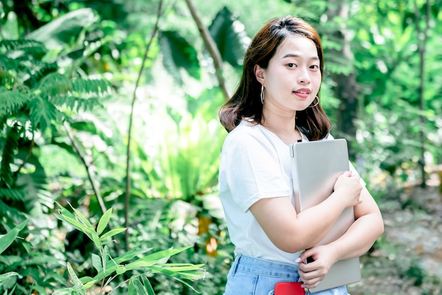 Портретные изображения азиатской привлекательной женщины, стоящей и держащей ноутбук