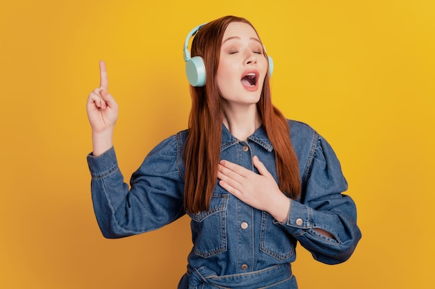 Portrait of independent lady wear earphones listen music close eyes sing song on yellow background