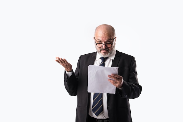 Portrait of Indian asian senior businessman holding or reading paper documents while standing against white background