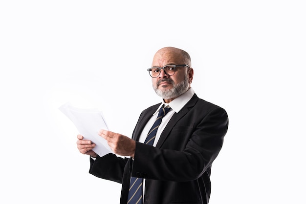 Portrait of Indian asian senior businessman holding or reading paper documents while standing against white background