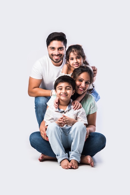 Portrait of Indian Asian young family of four sitting on white flour against white background, looking at camera