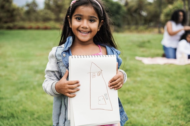 Ritratto di una bambina indiana che tiene un libro da disegno al parco cittadino focus sul viso