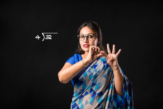 Portrait of Indian lady teacher in saree stands against green, white or blackboard 