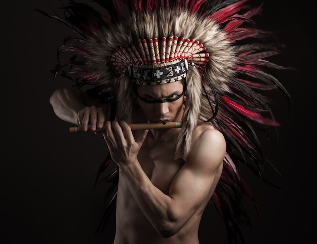 Portrait of the indian strong man posing with traditional native american make up. Playing flute