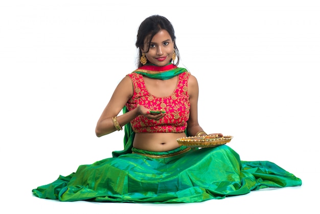 Photo portrait of a indian traditional girl holding diya, girl celebrating diwali or deepavali with holding oil lamp during festival of light on white surface