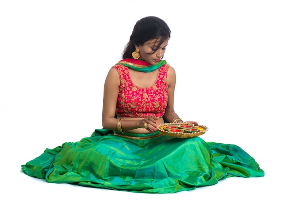 Portrait of a Indian Traditional Girl holding Diya, Girl Celebrating Diwali or Deepavali with holding oil lamp during festival of light on white surface