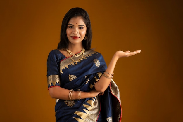 Portrait of Indian traditional young woman or girl presenting something showing copy space on her palm on a brown background