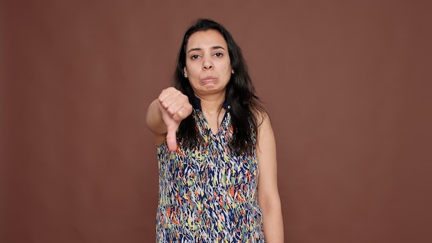 Portrait of indian woman giving thumbs down and showing\
disppointment about bad news. doing dislike sign and expressing\
refusal, rejection after failure and denial. disagreement.