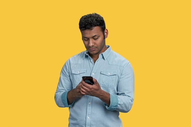 Portrait of indian a young man using smartphone isolated on vivid yellow background