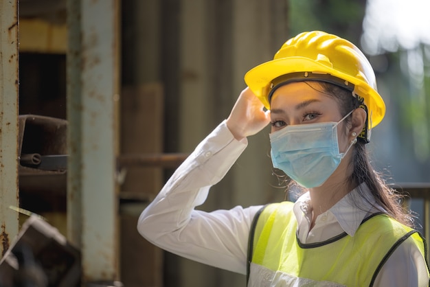 工場に立っているマスクを持つ産業女性エンジニアの肖像画。