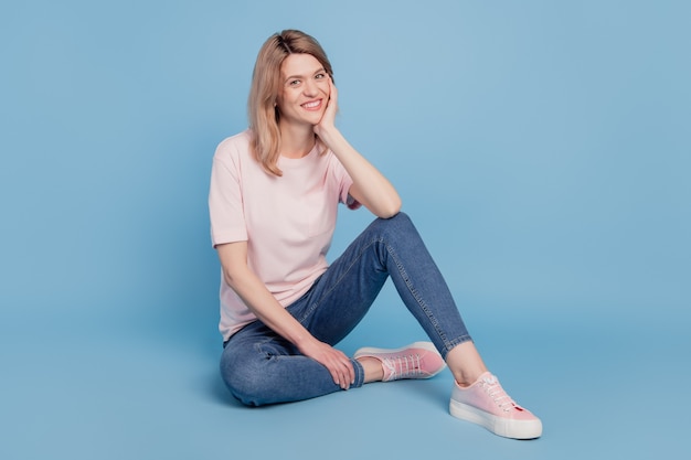 Portrait of inspired cheerful pretty girl sit floor posing rest on blue background