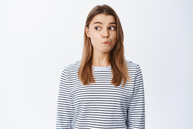 Portrait of intrigued blond girl checking out something interesting pucker lips and looking left with tempted face wants to try something white background