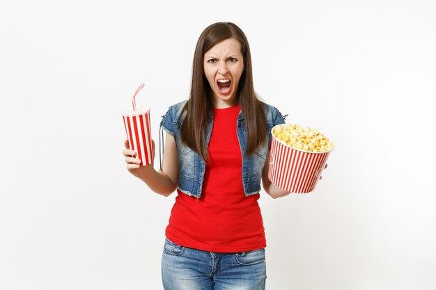 Portrait of irritated scared woman in casual clothes screaming watching movie film, holding bucket of popcorn and plastic cup of soda or cola isolated on white background. Emotions in cinema concept.