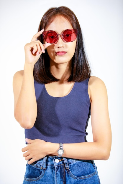 Portrait isolated closeup studio cutout shot of Asian female model in crop top shirt jeans and sunglasses smiling look at camera on white background