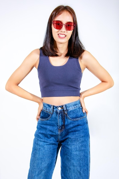 Portrait isolated closeup studio cutout shot of Asian female model in crop top shirt jeans and sunglasses smiling look at camera on white background