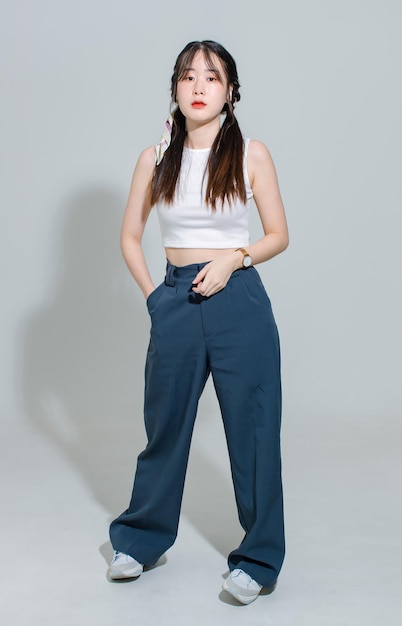 Portrait isolated cutout full body studio shot asian young pretty female fashion model with pigtails braids hair in fashionable sleeveless crop top standing posing look at camera on white background