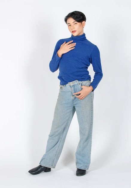 Портретная изолированная студия выреза в полный рост азиатской молодой модели-гея в джинсовой рубашке с длинными рукавами и джинсах с высоким каблуком в кожаных туфлях на высоком каблуке, стоящая и позирующая, глядя в камеру на белом фоне
