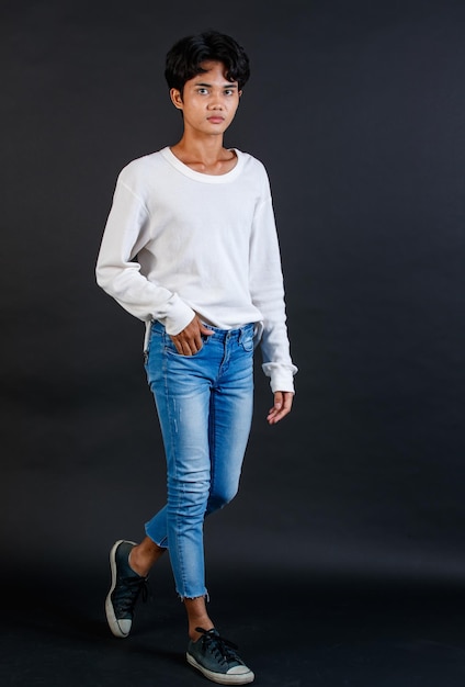 Portrait isolated cutout studio full body shot of Asian young LGBTQ gay glamour handsome male model in casual white long sleeve shirt jeans sneakers posing walking look at camera on black background