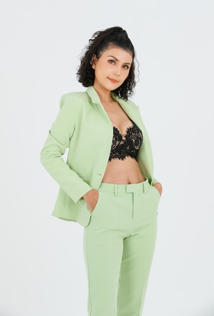 Portrait isolated cutout studio shot of Asian sexy curly hair fashion businesswoman in green suit with black lace lingerie crop top bra standing posing put hands in pants pockets on white background