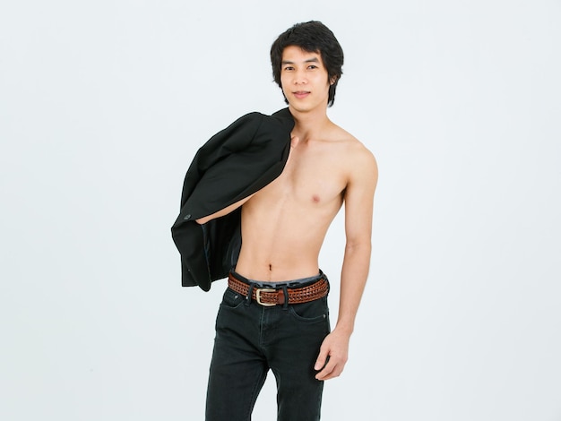 Portrait isolated cutout studio shot of Asian young handsome confident slim thin muscular shirtless teenager male model standing smiling posing placed suit blazer across shoulder on white background