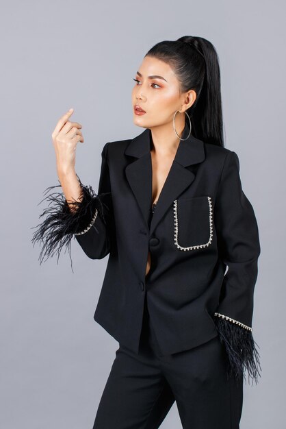 Portrait isolated cutout studio shot of Millennial Asian female elegant fashion model in black casual fashionable fur suit standing posing put hand in pants pocket look at camera on gray background