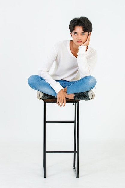 Portrait isolated studio shot Asian young LGBT gay happy handsome bisexual homosexual male fashion model in casual outfit sitting crossed legs on tall chair smiling look at camera on white background