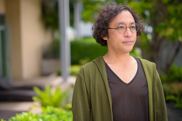 Portrait of Japanese man with curly hair wearing eyeglasses with nature in the rooftop garden outdoors